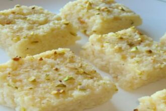 Homemade Kalakand garnished with chopped pistachios and almonds on a serving plate.